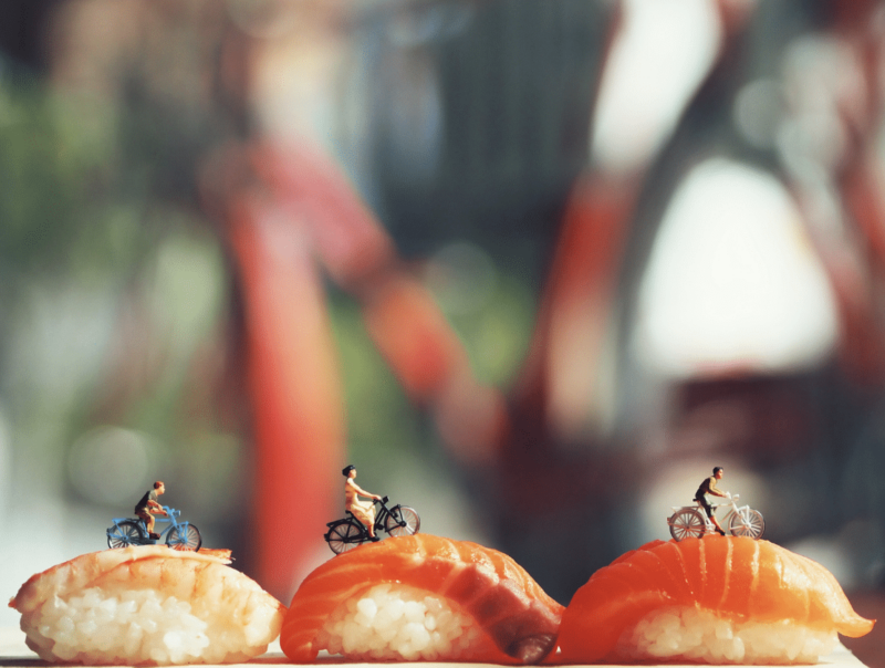 Miniature people riding bicycles on salmon sushi