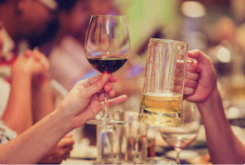 two peoples hands toasting beer and wine